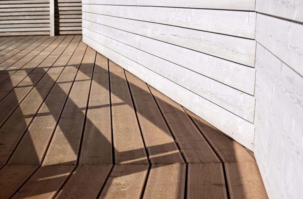 A wooden deck with white wooden siding and shadow patterns cast across the surface, creating geometric shapes in natural light.